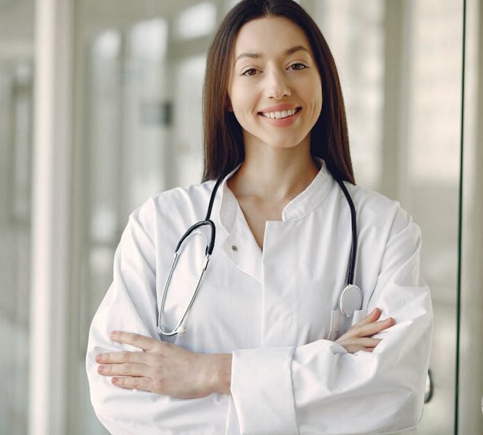 Portrait of a smiling female doctor with arms crossed and stethoscope in a hospital corridor.